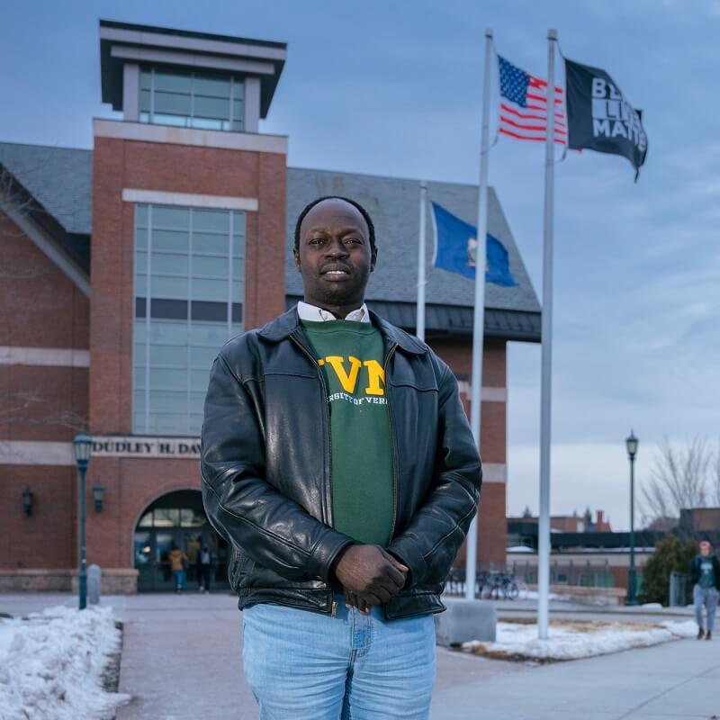 RSENR Recruitment and Retention Coordinator Akol Aguek standing in front of the Davis Center, a Black Lives Matter flag and an American flag is waving in the background