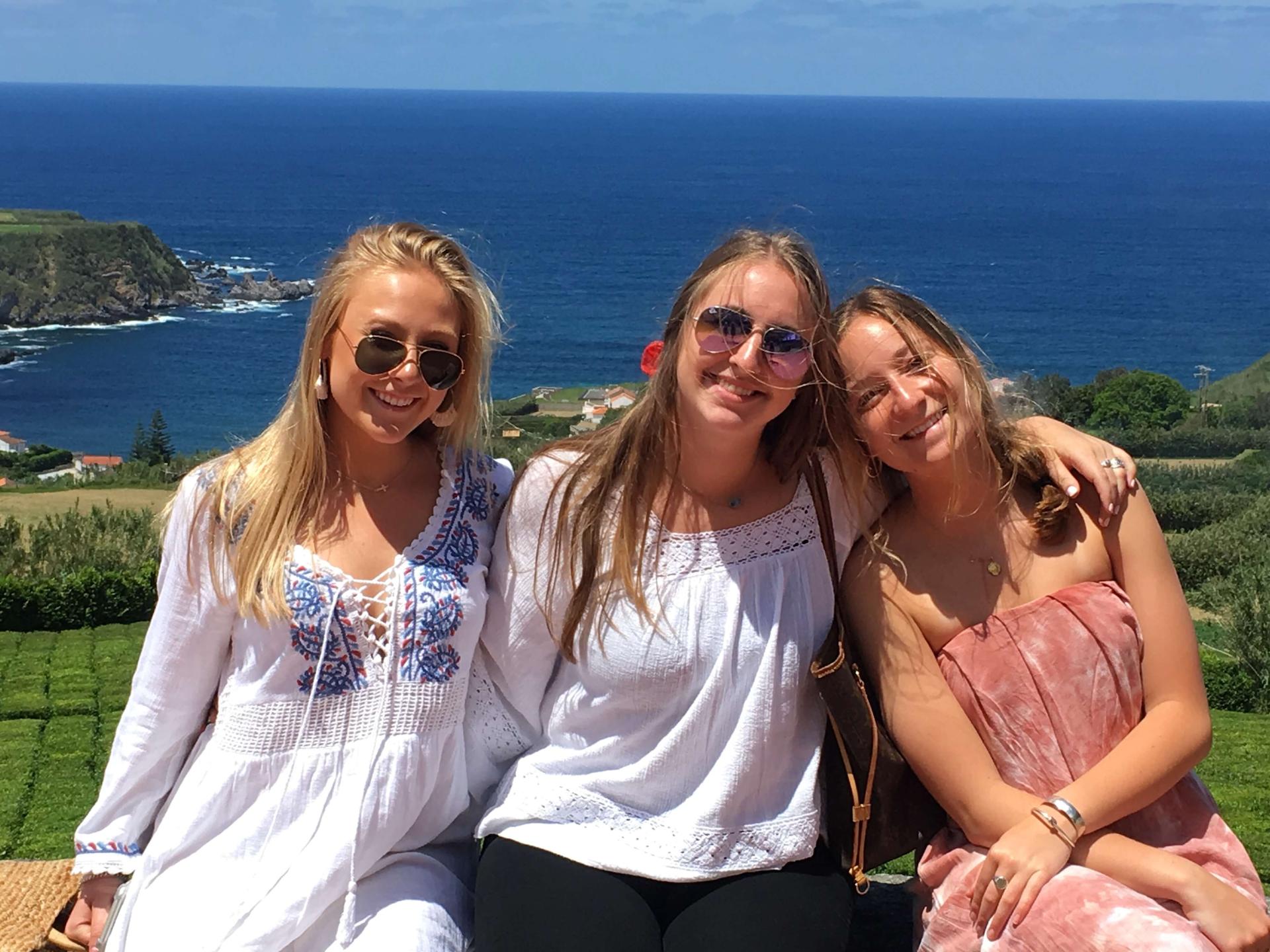Three students smiling in the sunshine in the Azores Islands of Portugal with the ocean in the background.