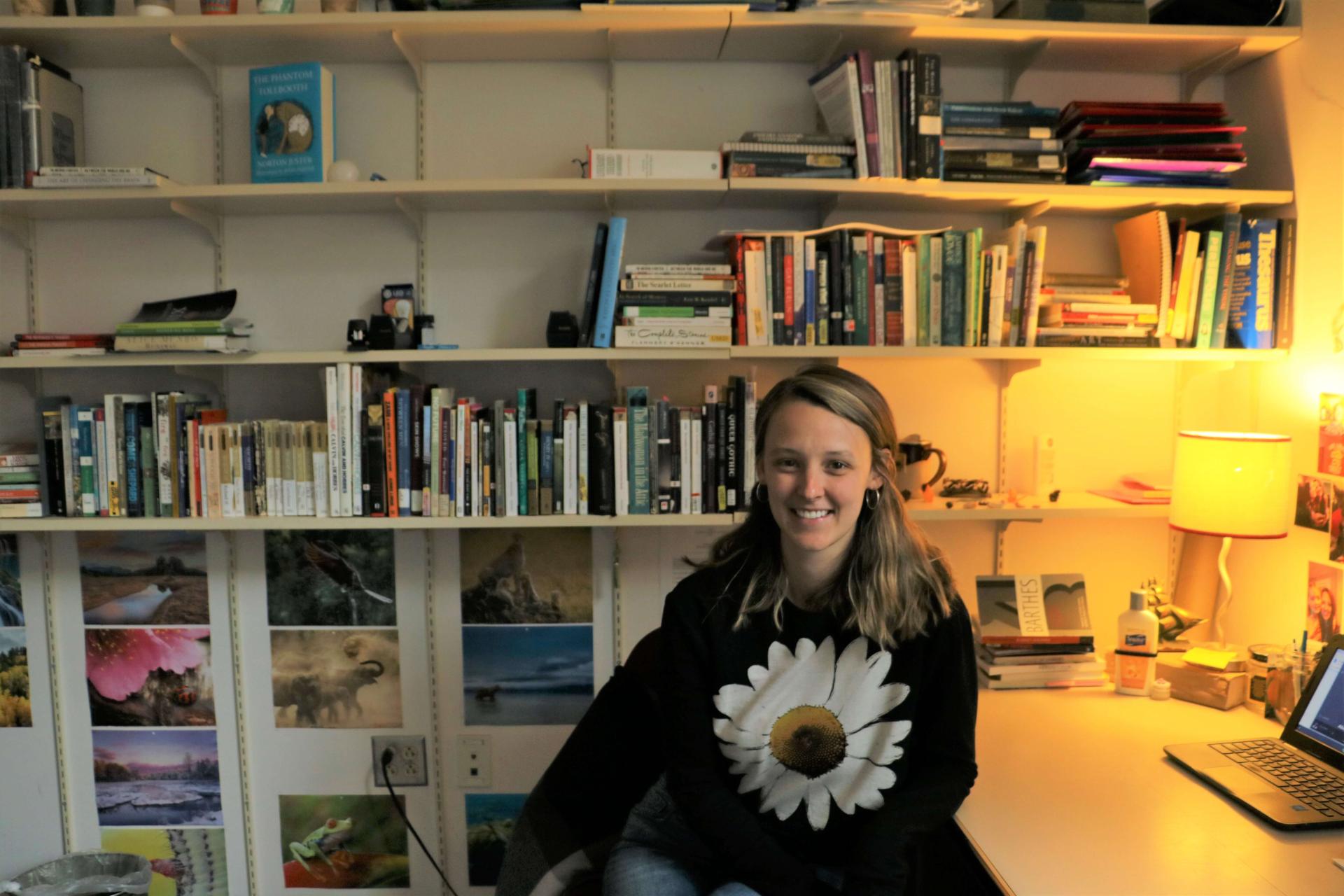 A student sitting at a desk, working on a laptop, surrounded by bookshelves.