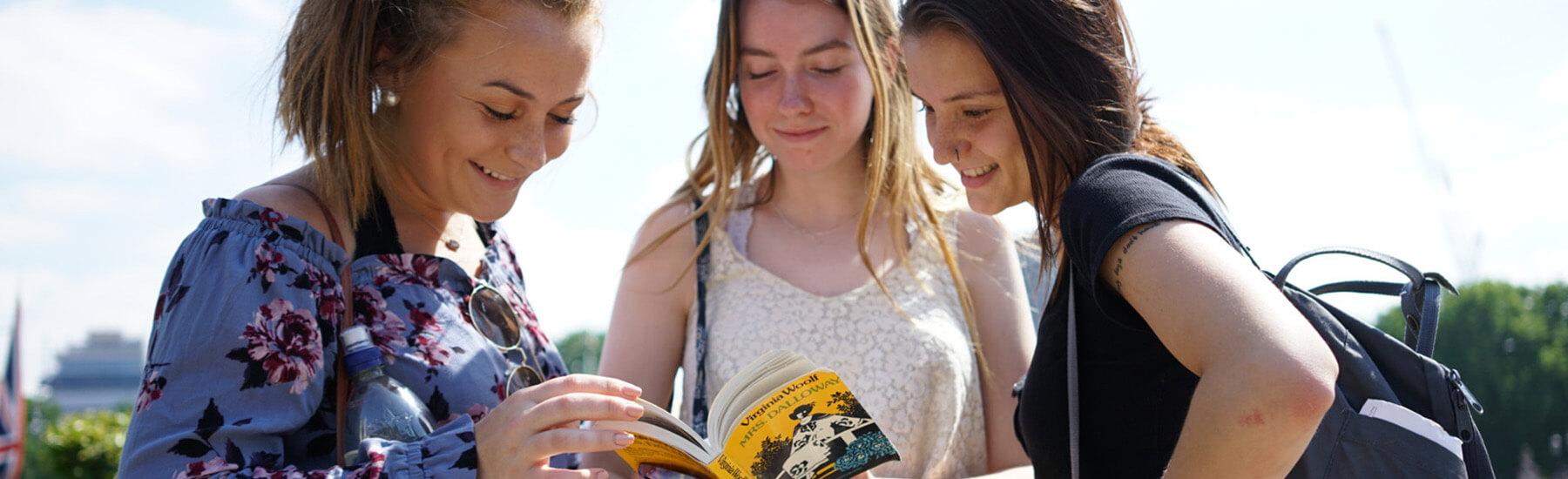 Group of three young women reading a book.