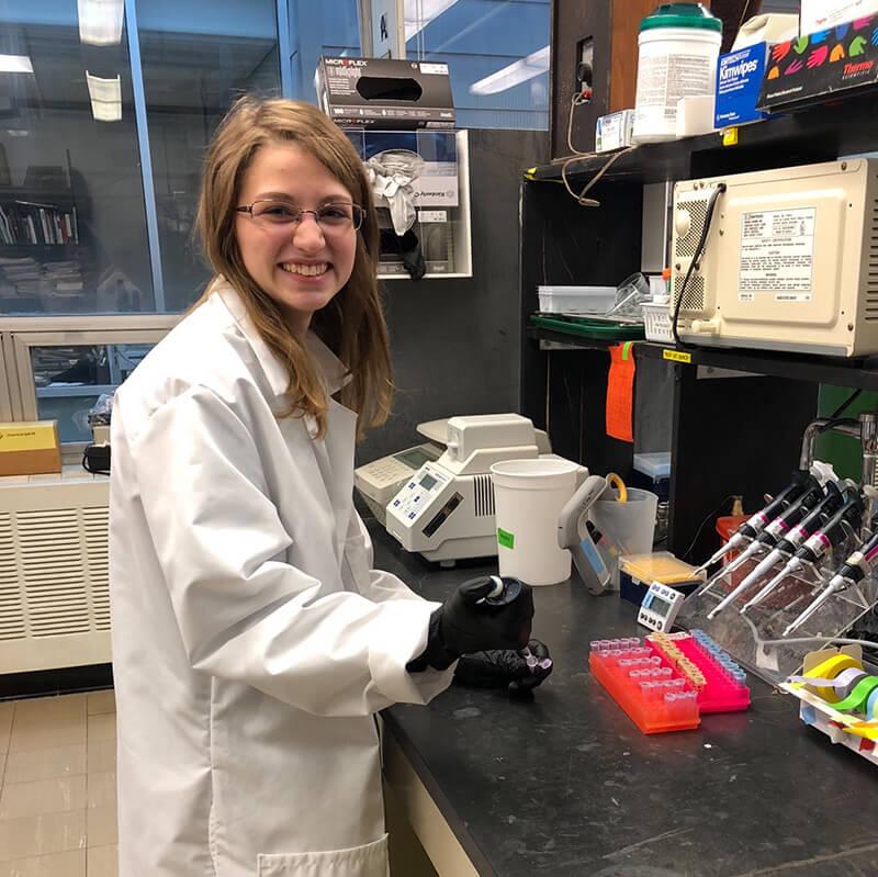 A student wearing white coat working in lab
