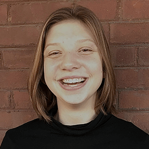 a smiling young woman standing against a brick wall