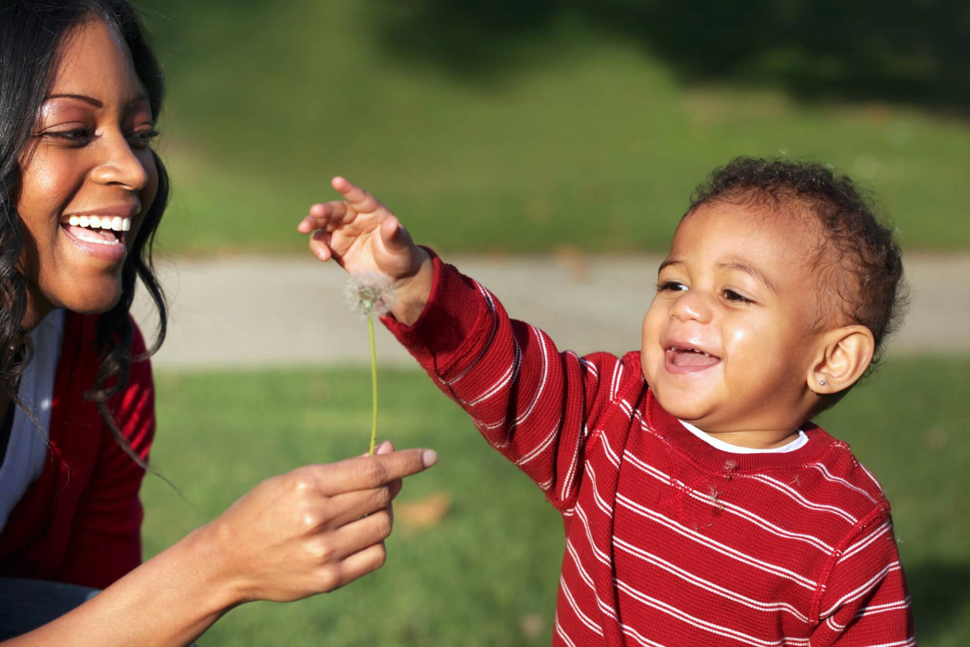 Mother and toddler laughing and playing together outdoors in nature.