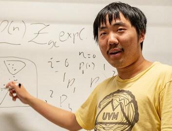 Jiangyong Yu pointing at whiteboard with math on it.