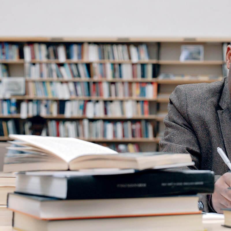 person at a library desk taking notes with books