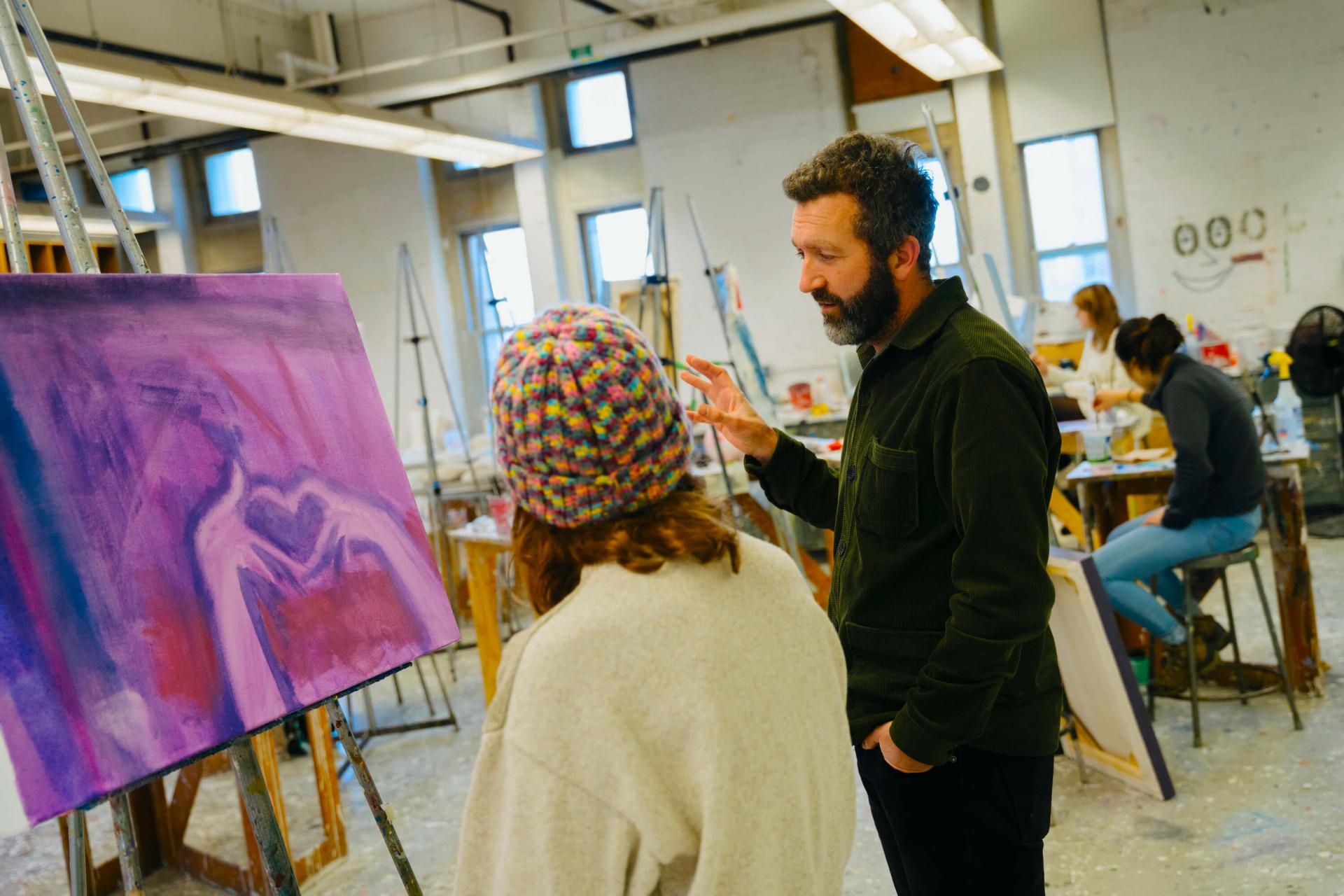 Mentor talks with a student about her painting in a studio setting.