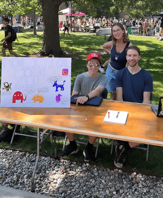 Three individuals seated at a table with a sign in front of them