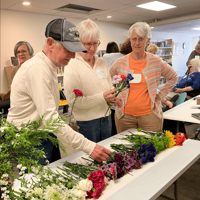 Three people participating in flower arranging from table of flowers