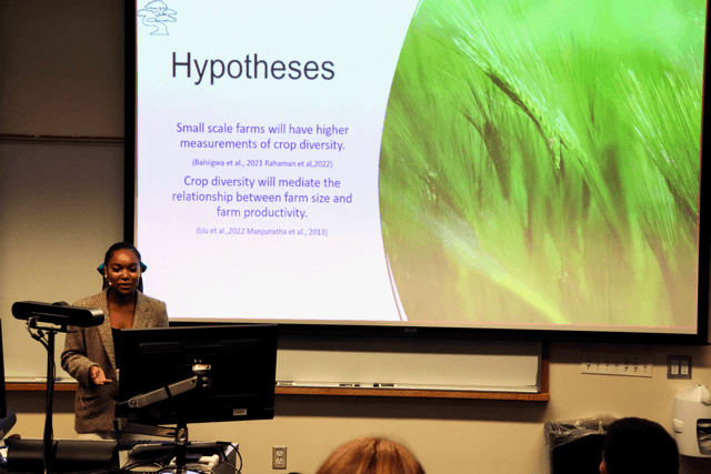 Graduate student giving a presentation with a slide that reads "Hypotheses"