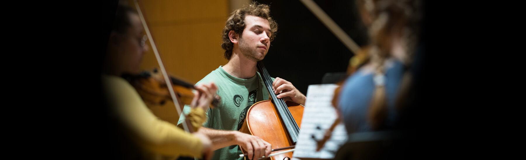 Musicians playing the cello and violin surrounded by a group of people 