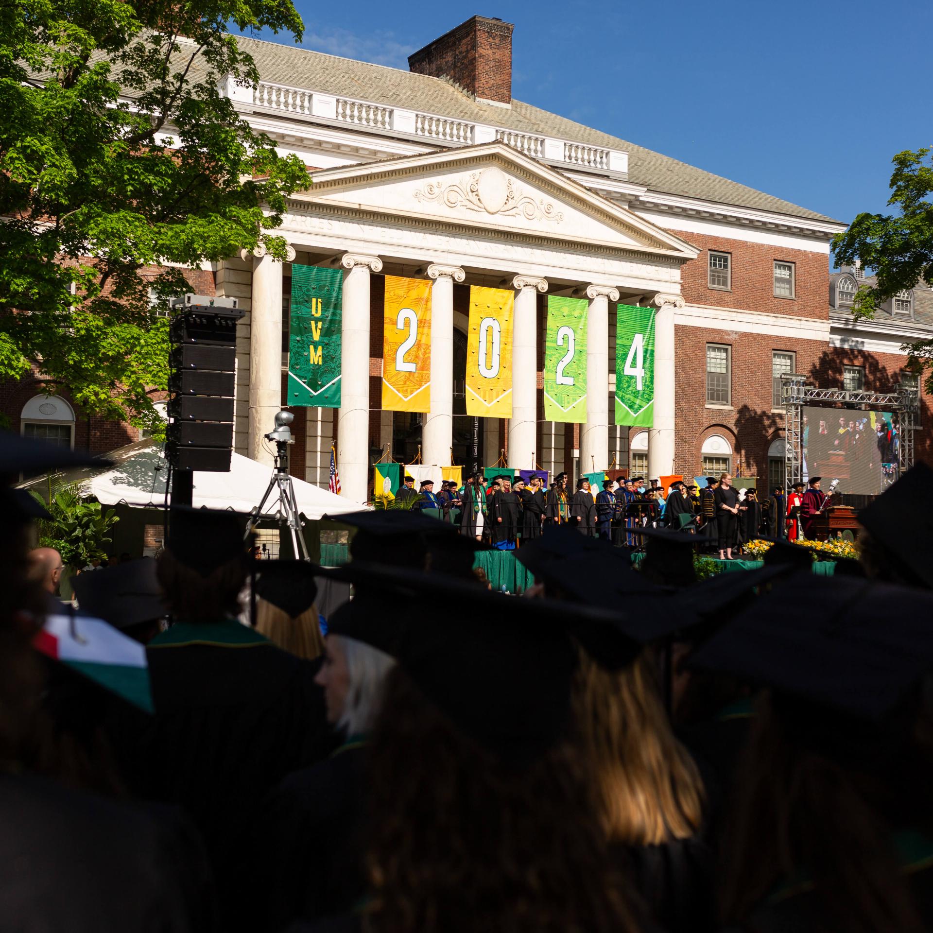 Commencement Banners displaying 2024 hanging on the Waterman building with crowd of students in front of it.