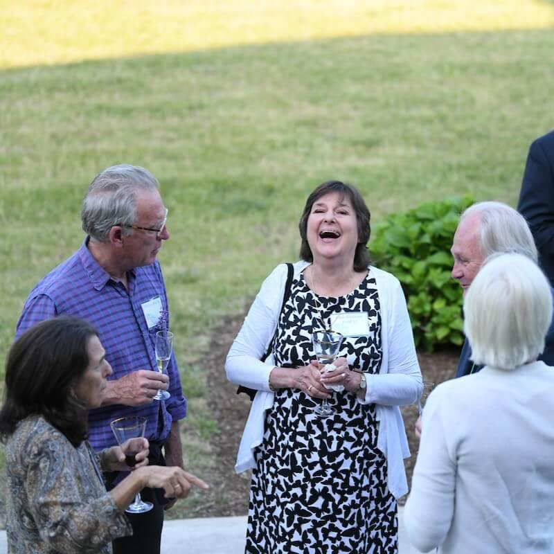 Alums laugh and talk on the lawn of the Alumni House