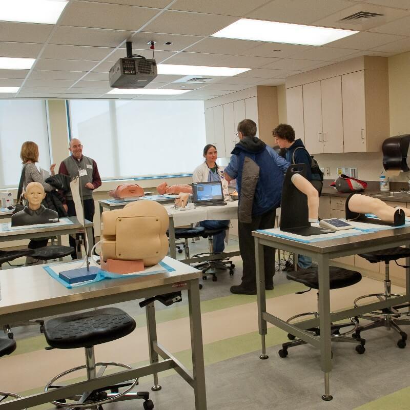 Faculty speak with students in the task trainer room