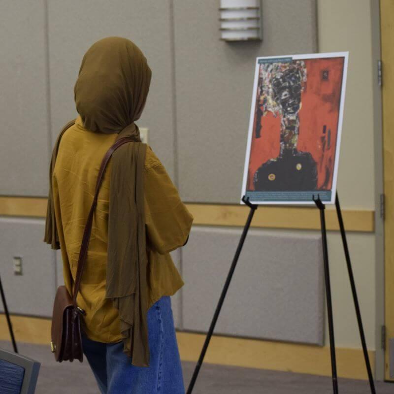 woman wearing a hijab looking at a painting on an easel