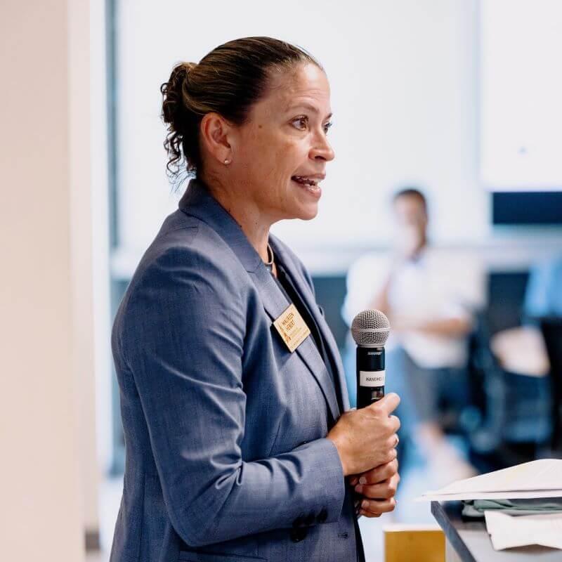 Woman standing at podium and speaking while holding a microphone