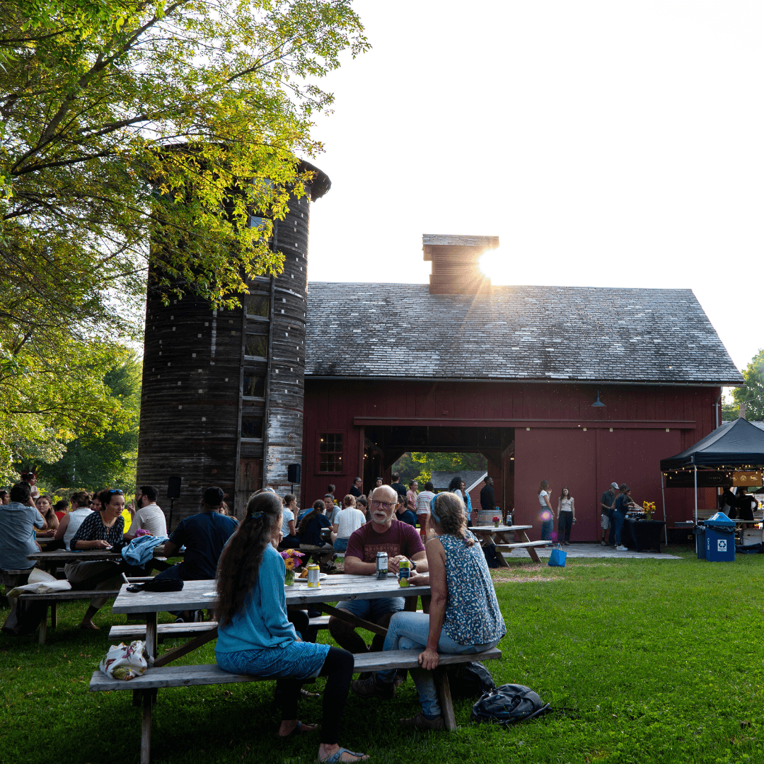 Sunsetting over a barn with people eating at picnic tables in foreground
