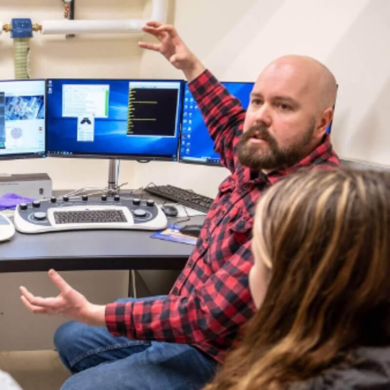 A person sitting in front of a computer using arms and hands to explain something to others.