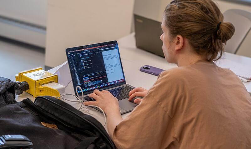 A student drafting computer code on a laptop