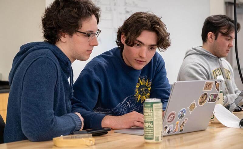 Two students sitting at a table looking at a laptop screen.