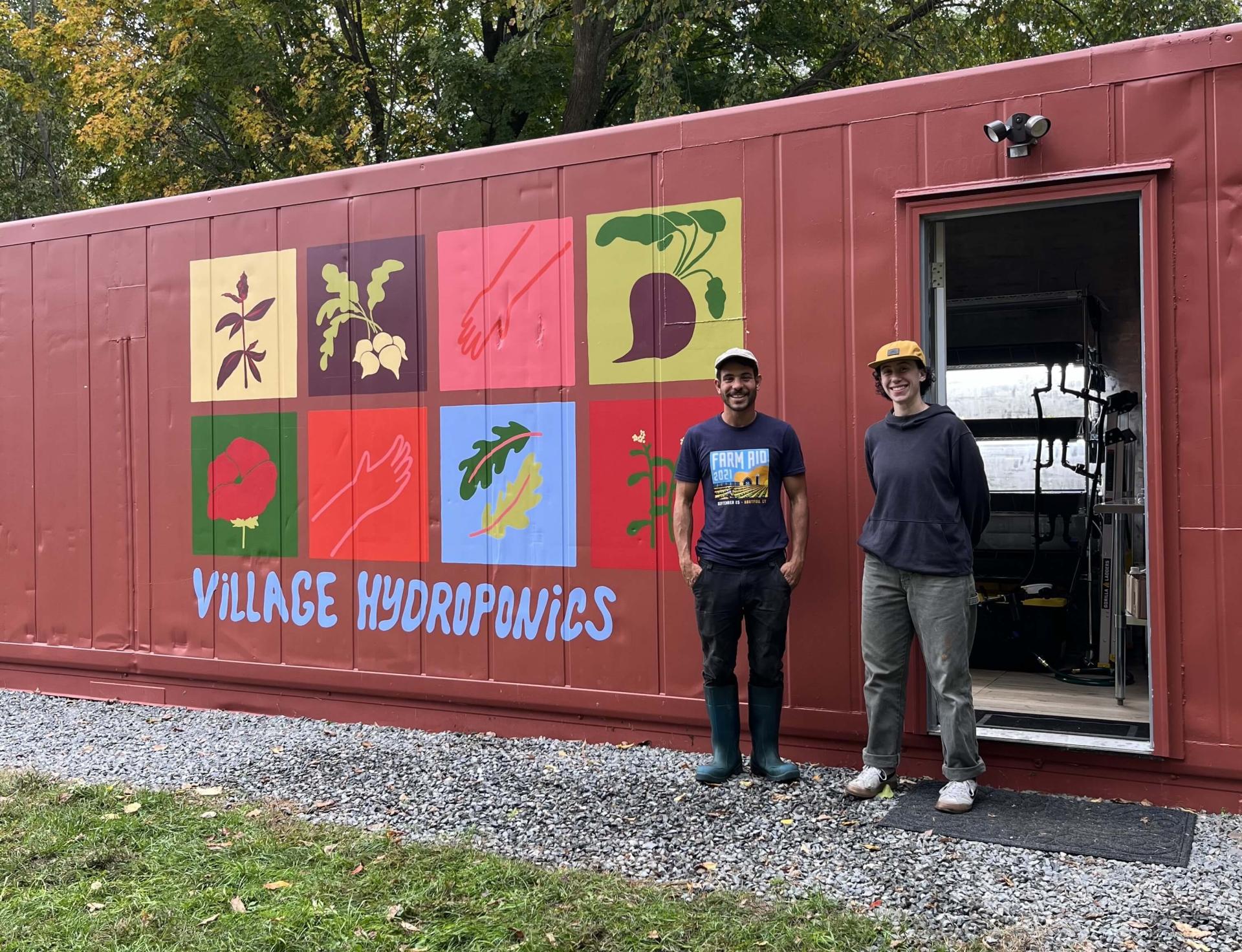 Photo of two people in front of a shipping container converted to hydroponics grow area.