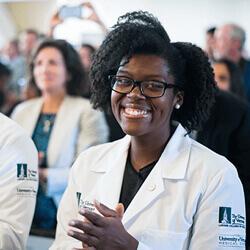 A smiling black, female medical student gets her white coat.