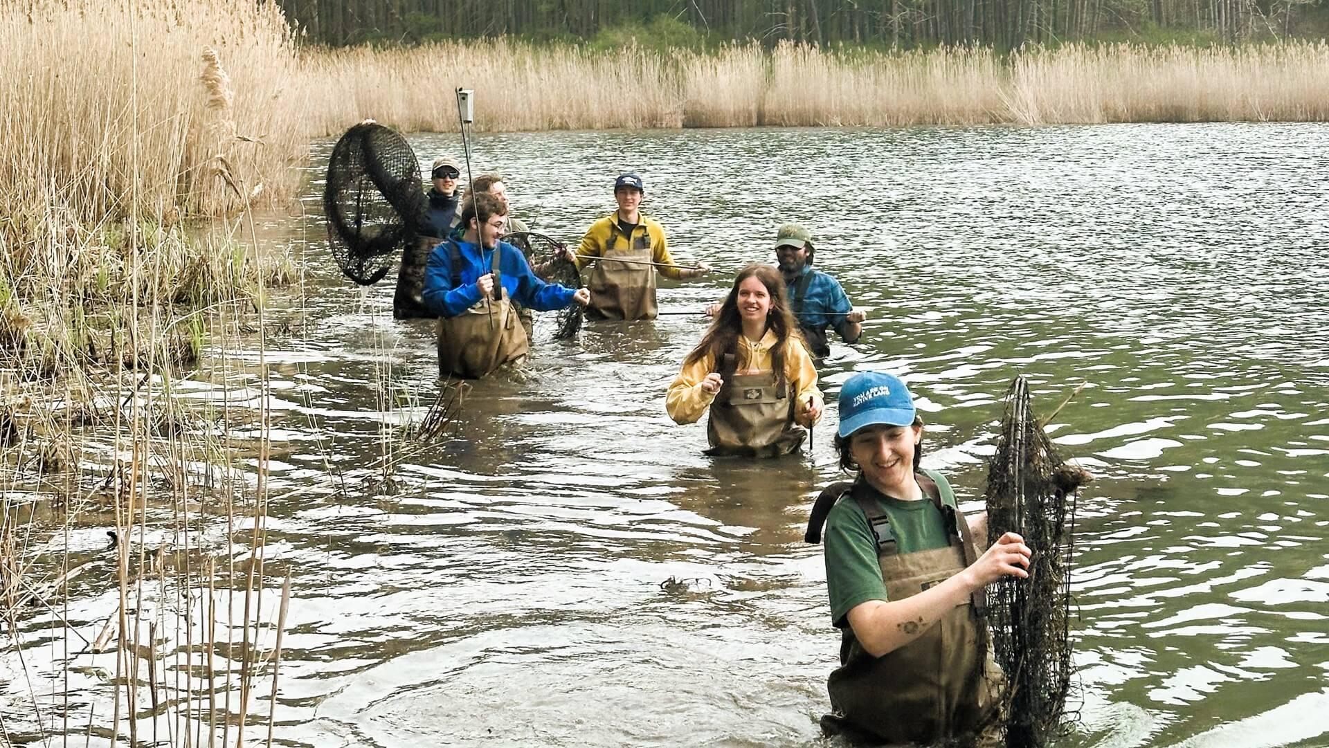 Students walking through waist-deep water carrying turtle traps