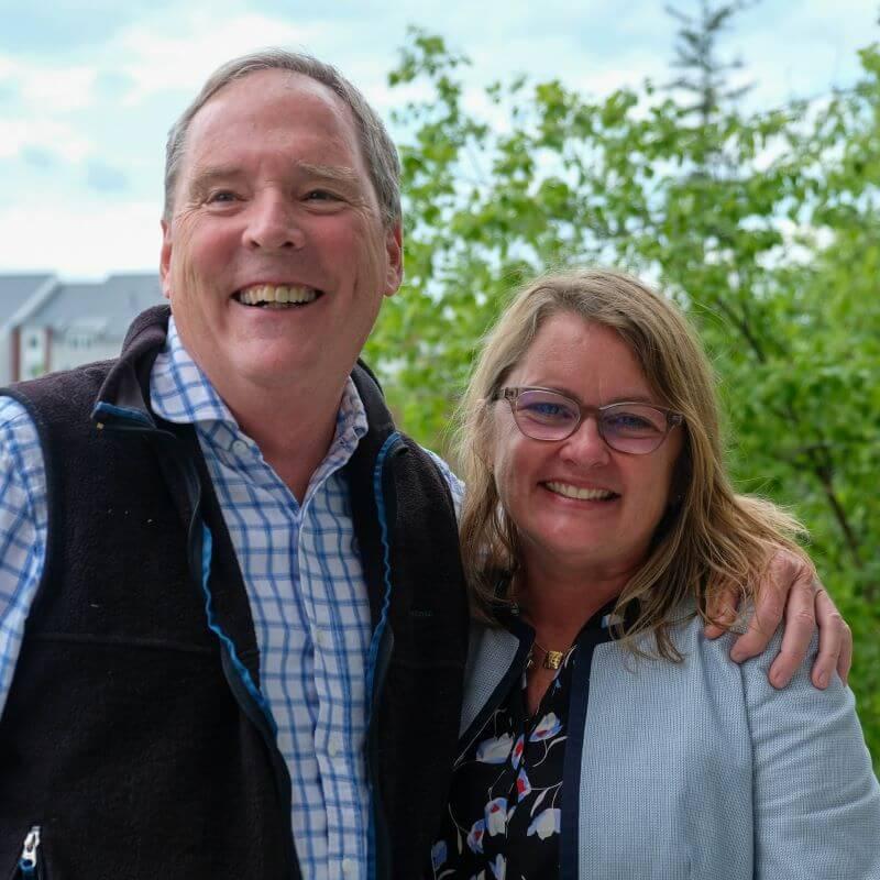 2 researchers posed together smiling outdoors, in front of green foliage.