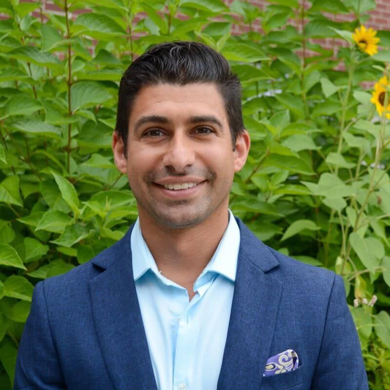 Headshot image of the researcher outdoors, posed in front of green foliage.