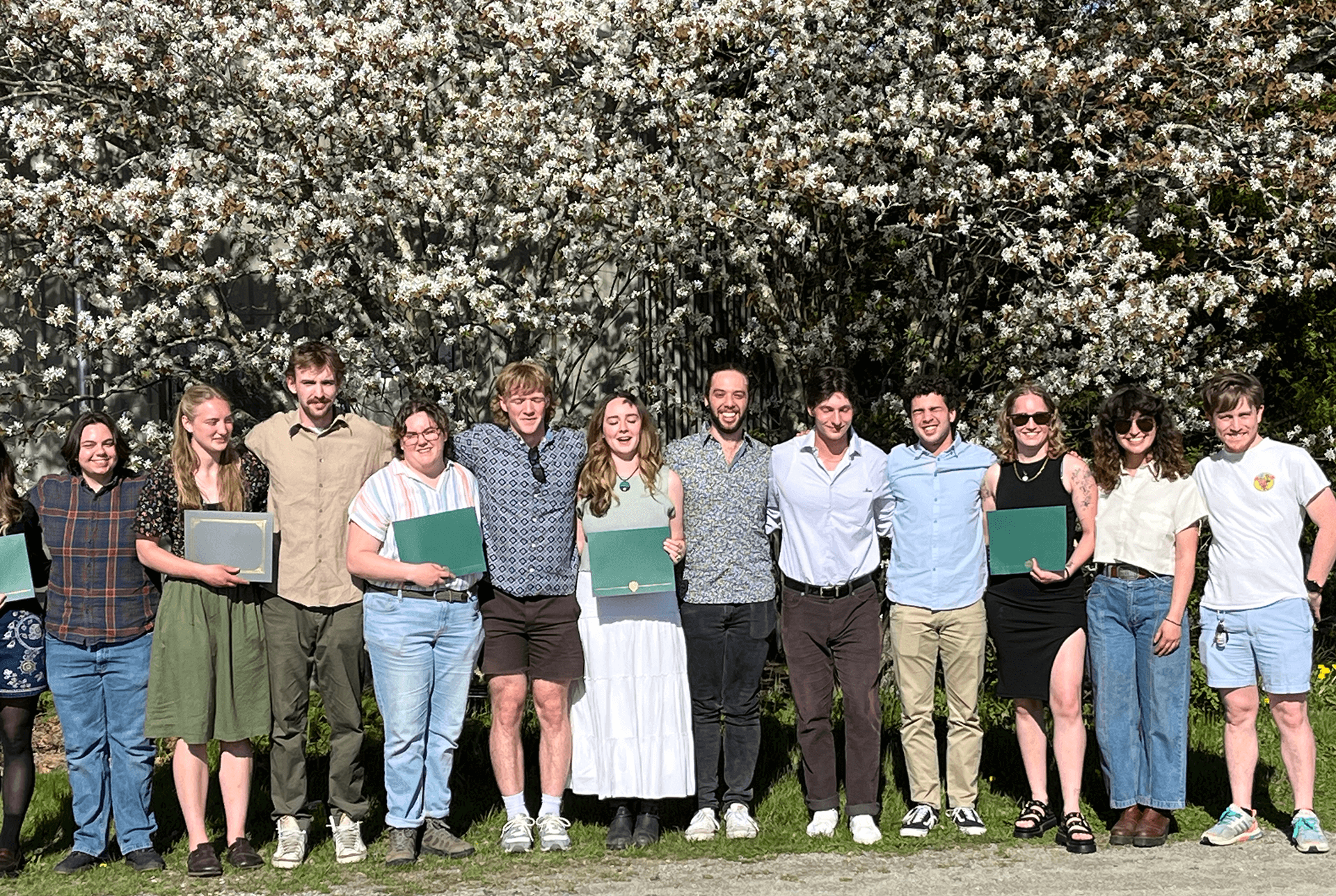 Students with awards standing in a row in front of flowering trees