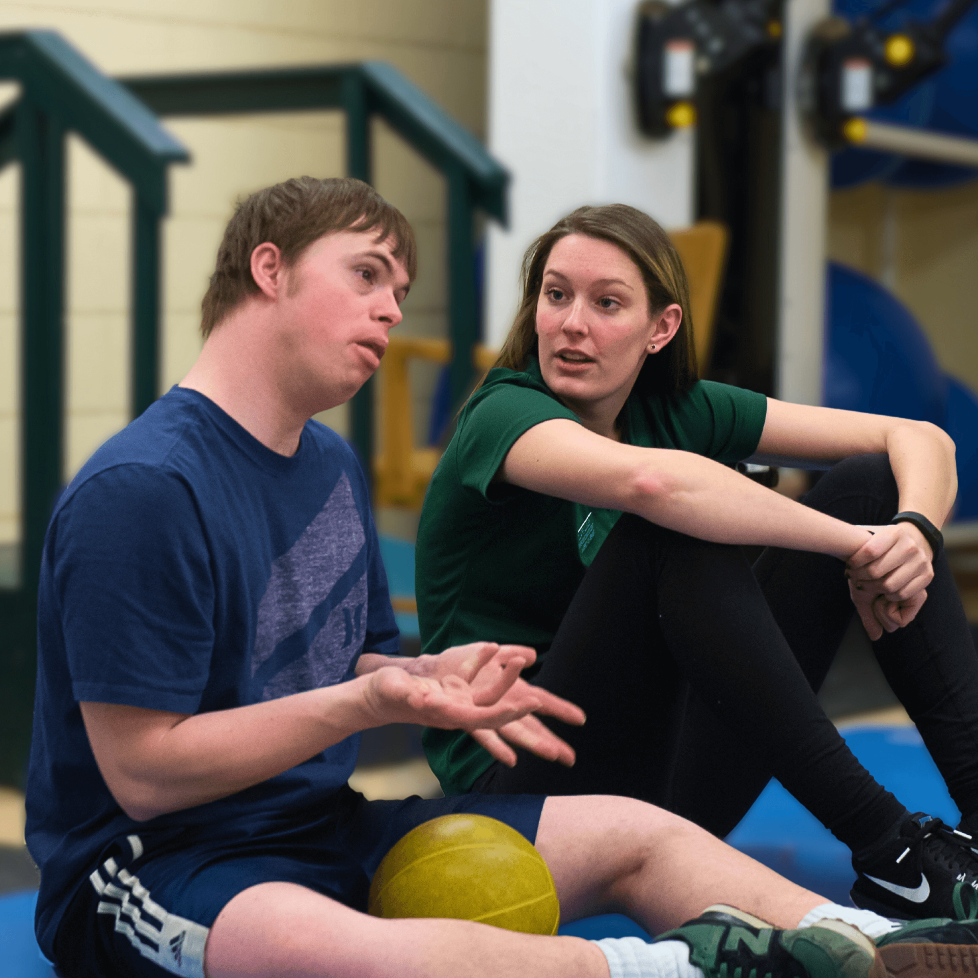 two students sitting on a mat in a gymnasium