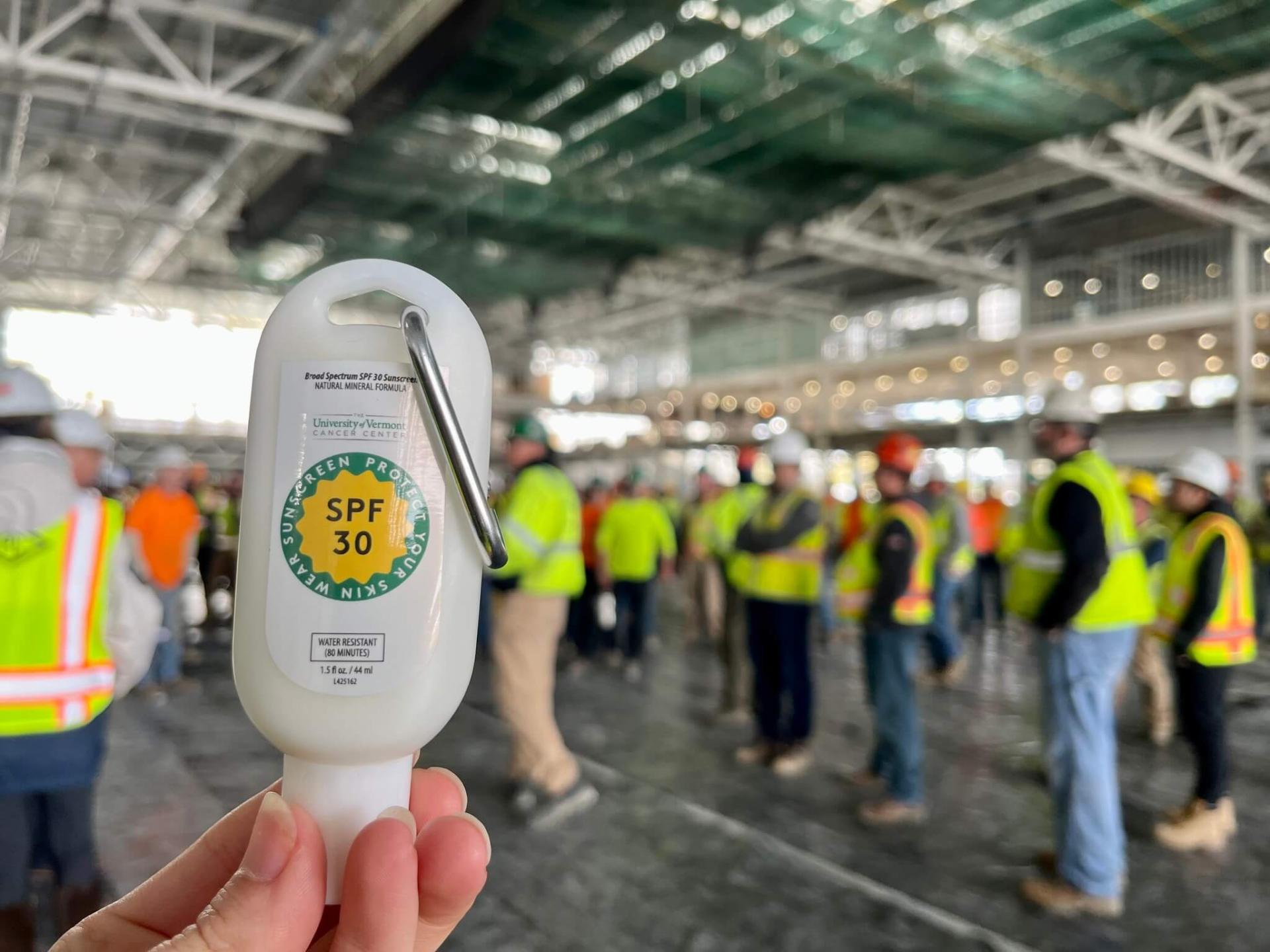 Travel size SPF 30 branded with the UVM Cancer Center logo, construction workers in the background