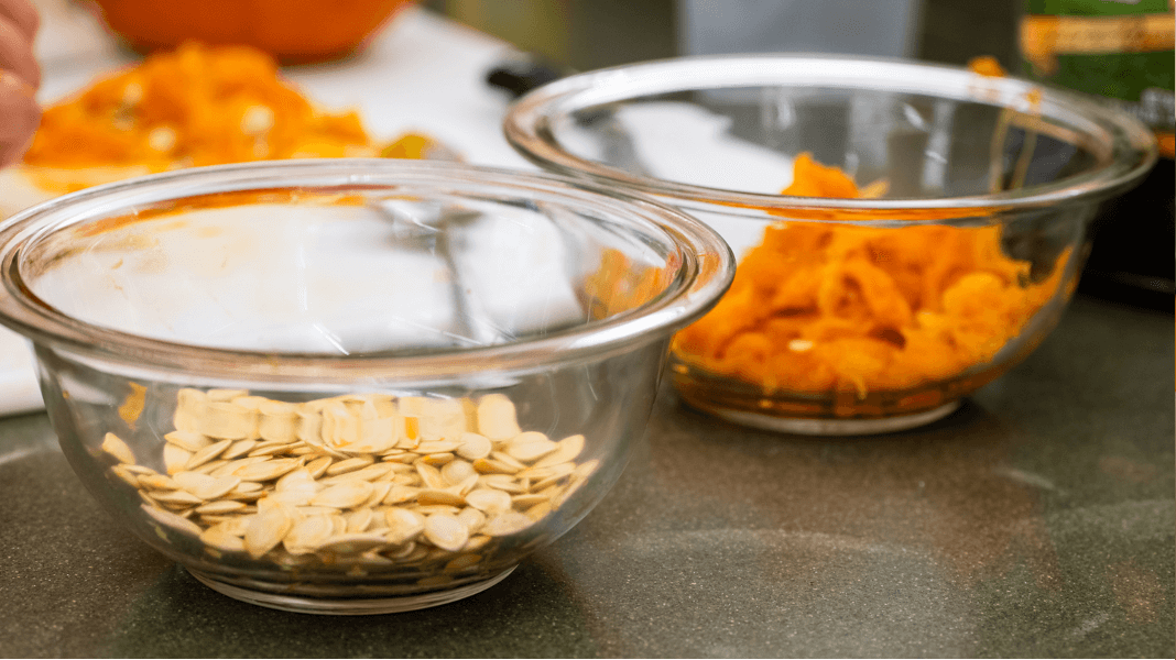 Two glass bowls, one with pumpkin seeds and the other with pumpkin pulp