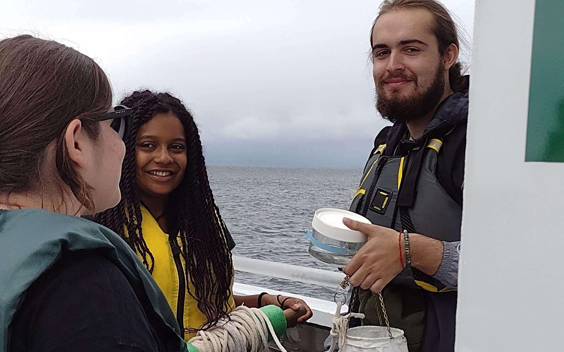 Three people on a boat, engaged with a container, navigating through serene waters under a bright sky