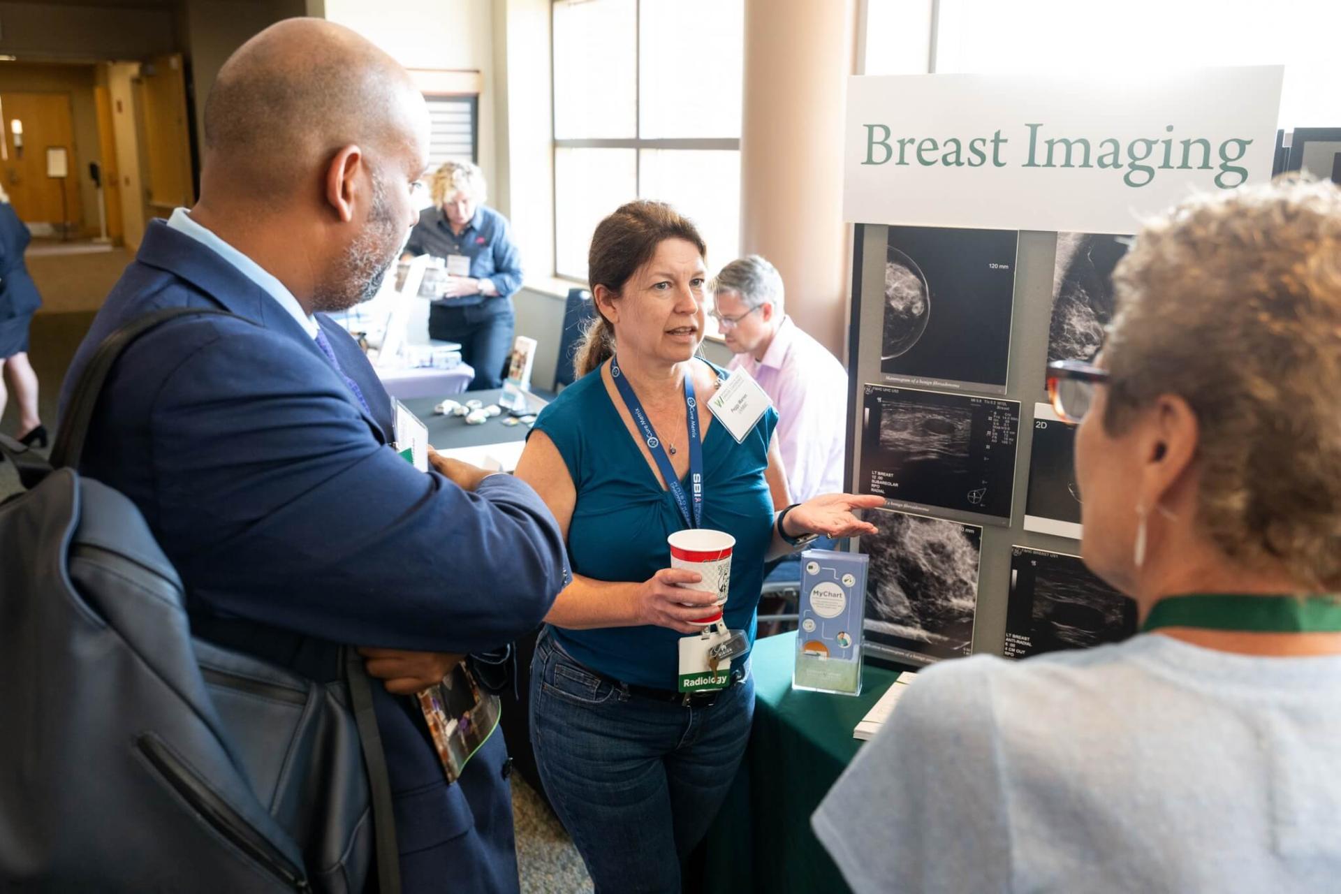 Three people in front of a breast imaging poster