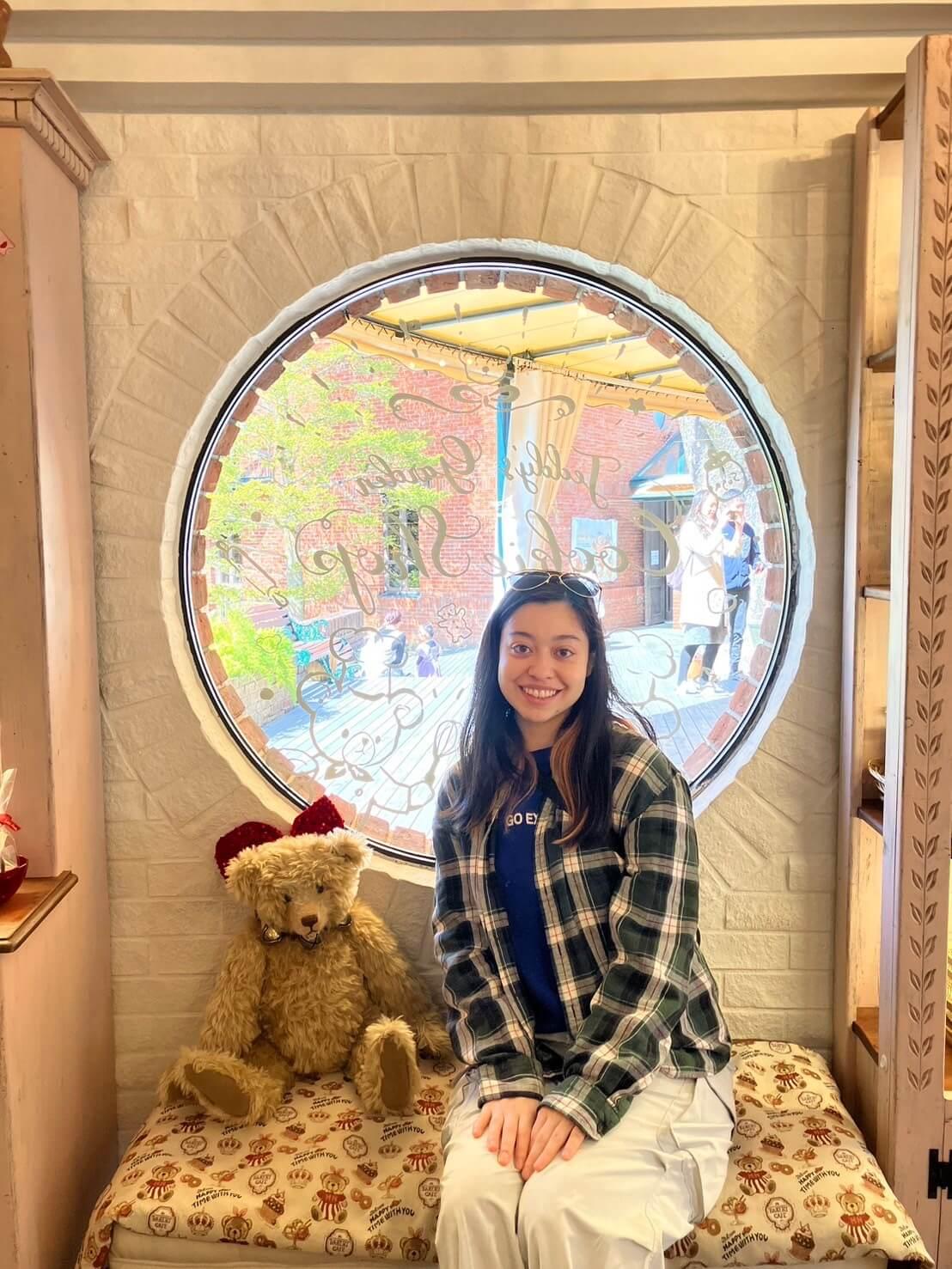 A woman sits on a bench, next to a toy teddy bear