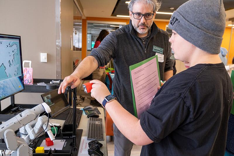 Professor Luis Espinosa shares some of UVM robots with an interested student