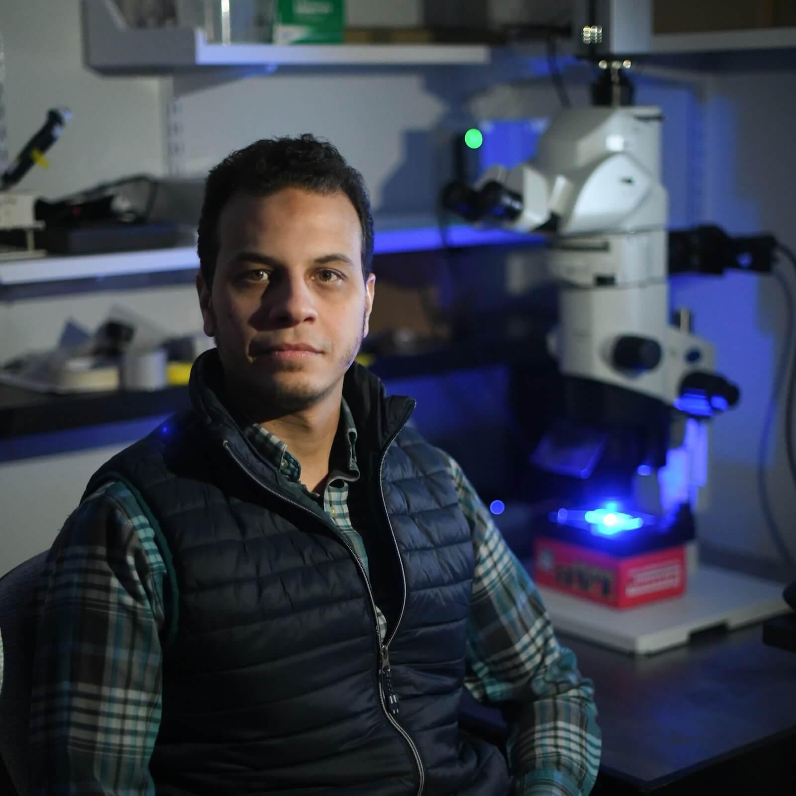 Researcher sitting in the lab with a microscope in the background