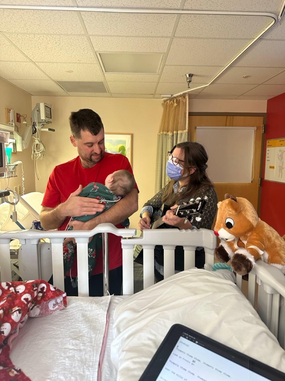 Man holding a baby and singing while a music therapist plays guitar