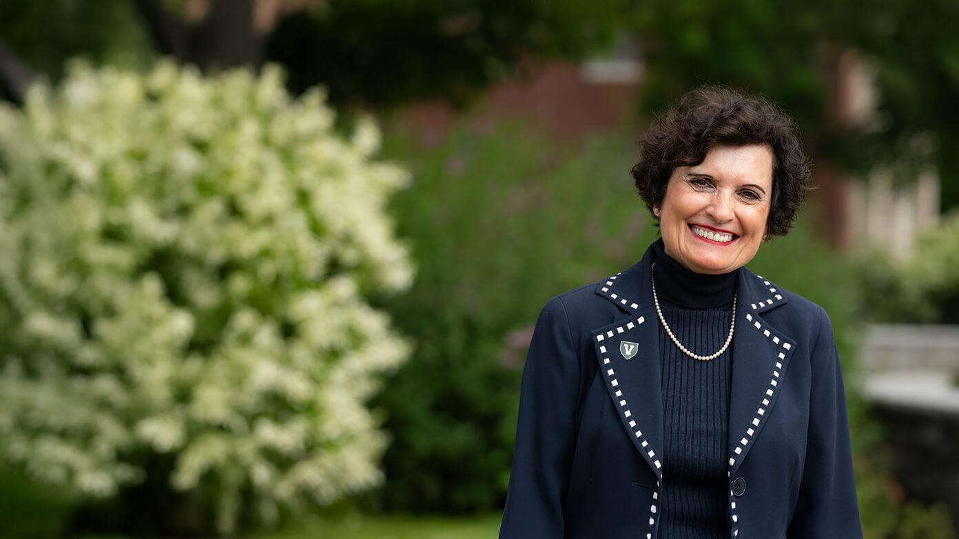 uvm president in a black blazer smiling while standing in front of greenery