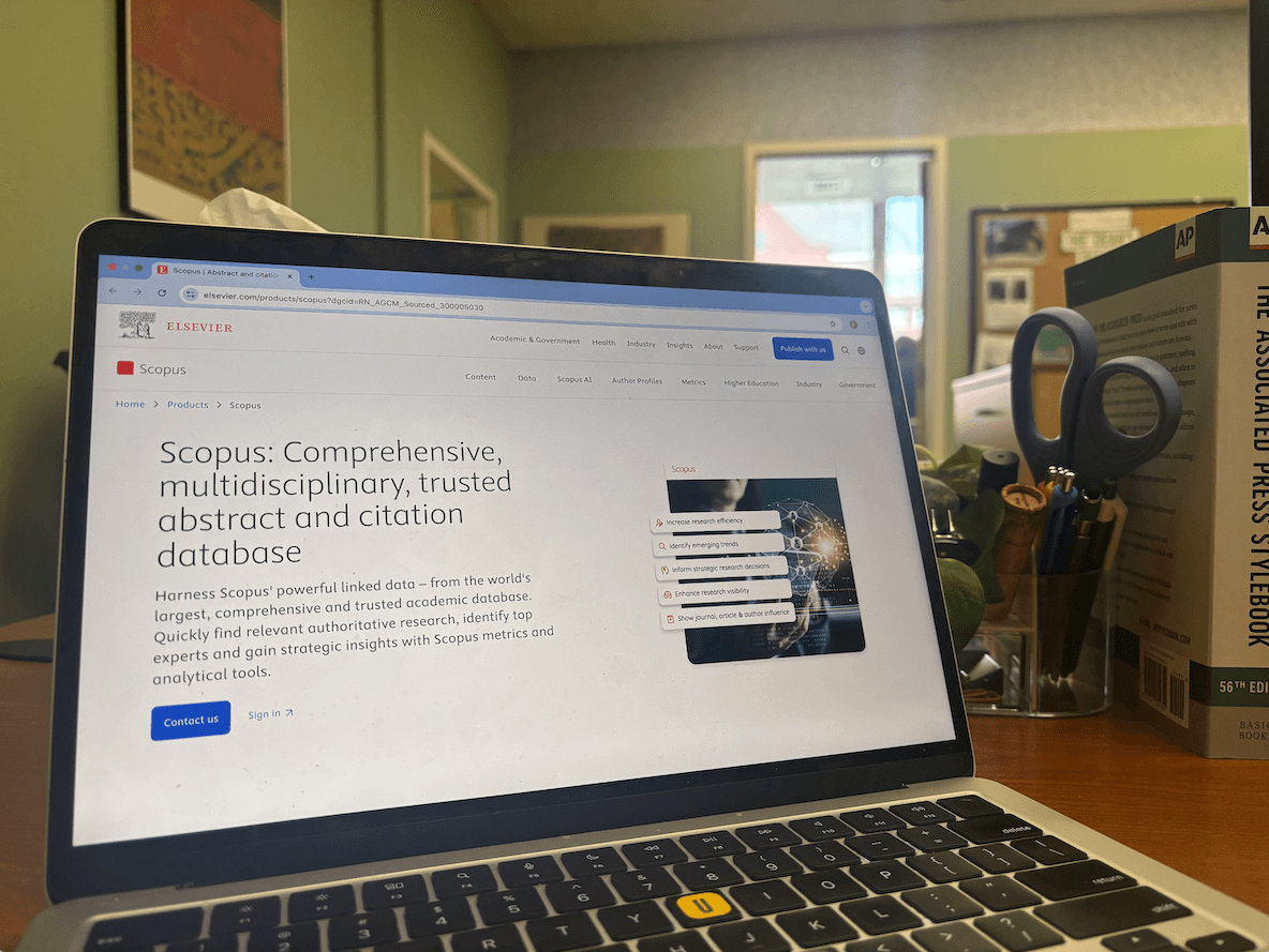 A laptop is open to a screen that says "Scopus: Comprehensive, multidisciplinary, trusted abstract and citation database."