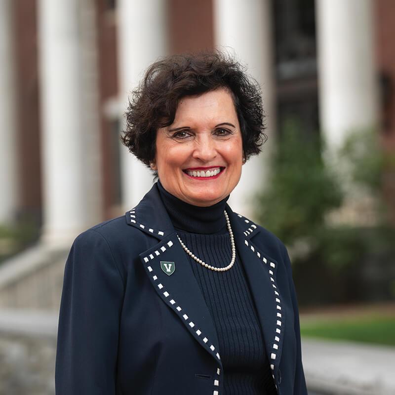 photo of patricia prelock in a black blazer with white dotted trim standing in front of the columns of the waterman building
