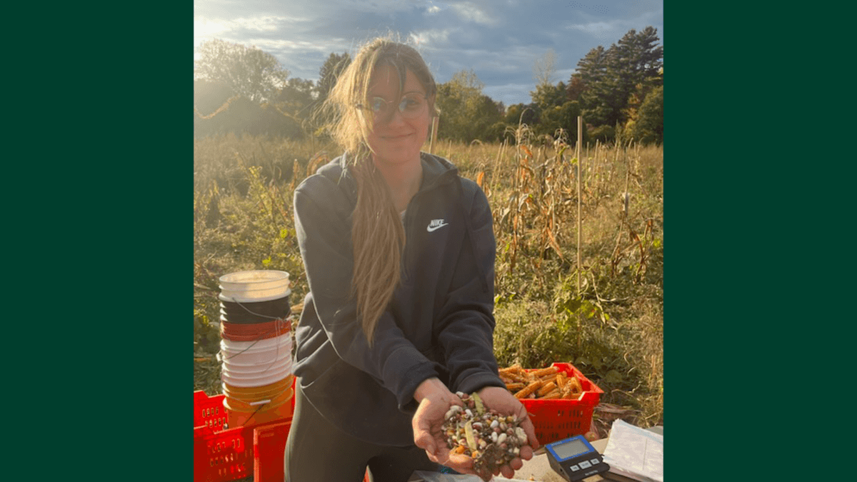 Bailey Kretzler in a field holding corn, beans, and squash seeds
