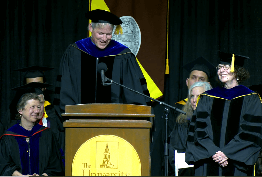 Interim Dean Allan Strong honoring Clare Ginger at the 2024 graduation celebration - both are on stage and wearing regalia