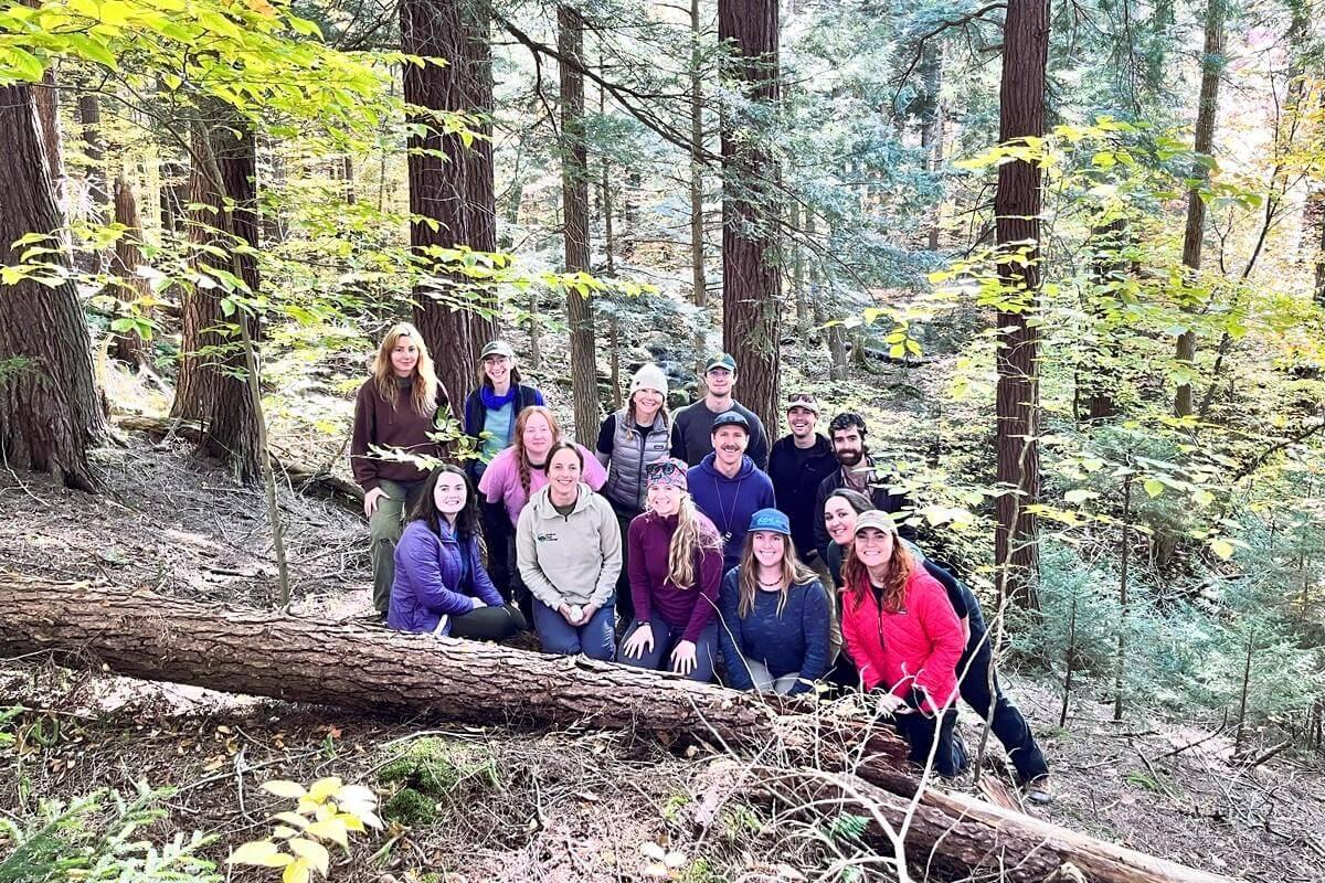 The group of students all together among standing and fallen trees in the forest