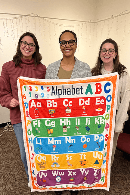 Three women holding an alphabet kids blanket