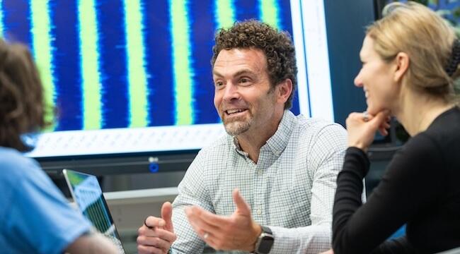 Chris Danforth sitting at a table talking and gesturing with his hands