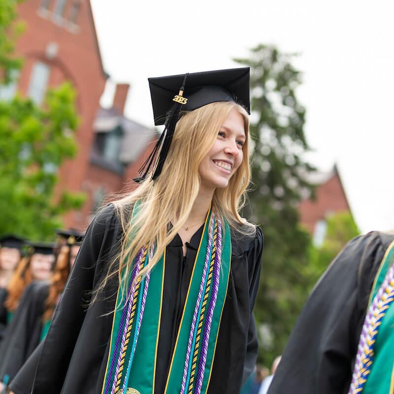 A person in a graduation gown smiles joyfully while walking