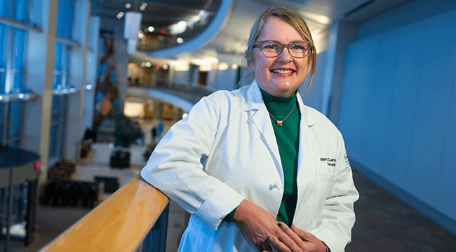 a woman in a white coat smiling leaning on a railing