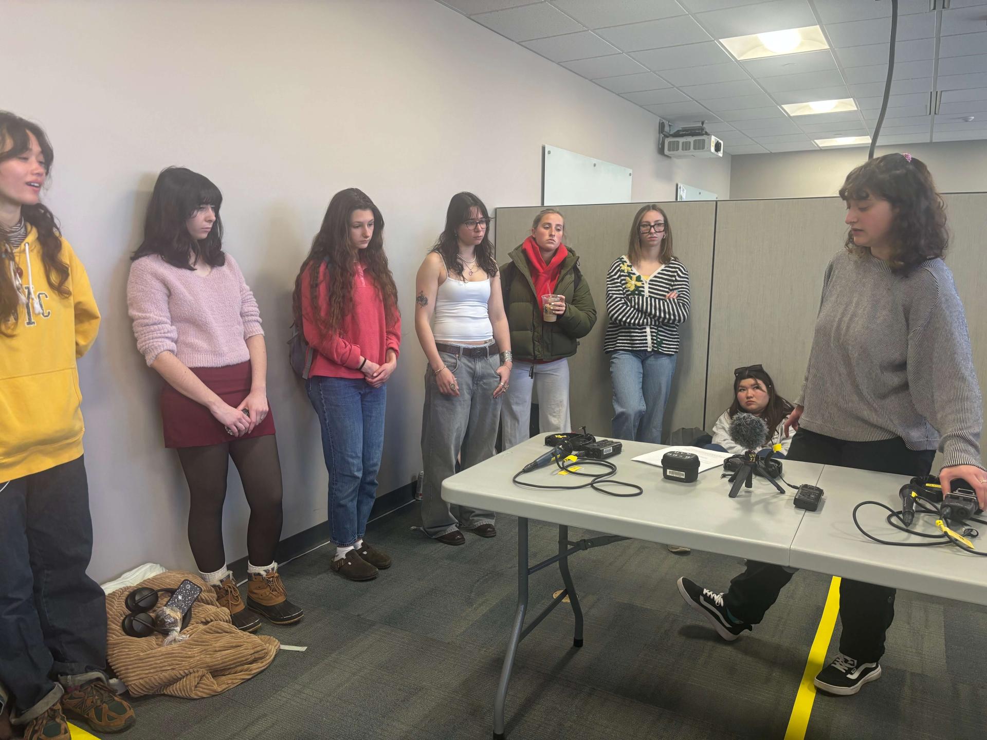 Students surround a table holding media equipment as Clemma Prince gestures toward the equipment.