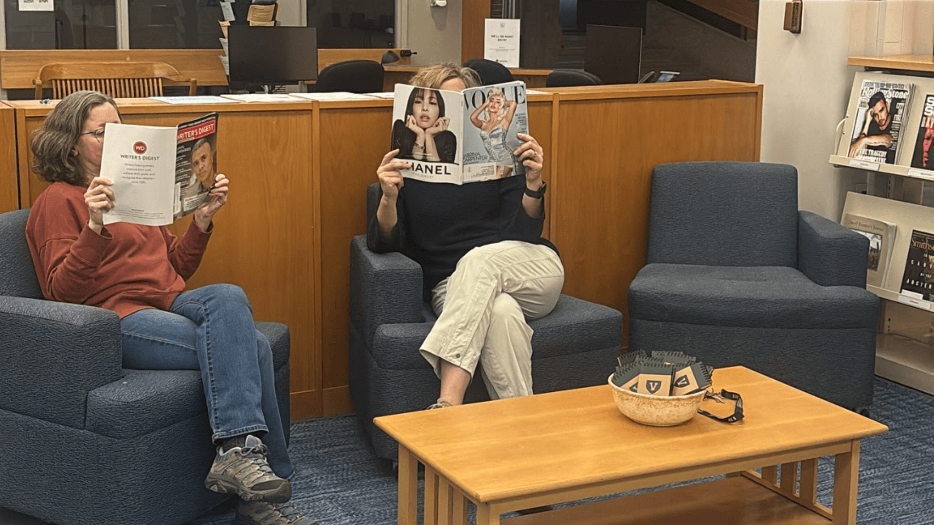 Two people sitting in comfy chairs reading magazines.